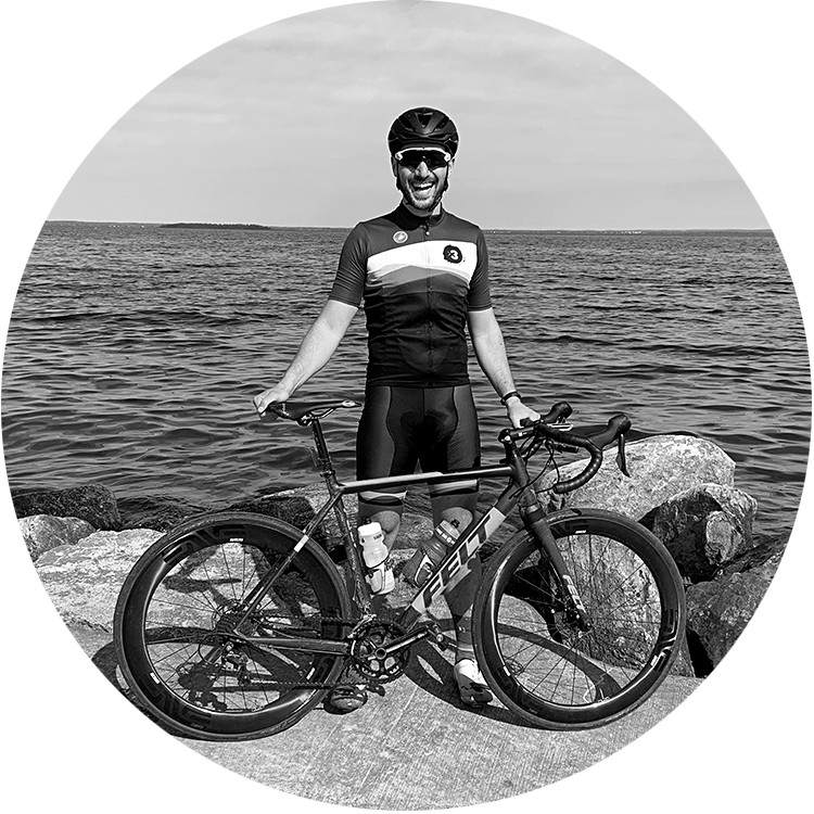 Coach Michael standing with his bike, smiling in front of a lake